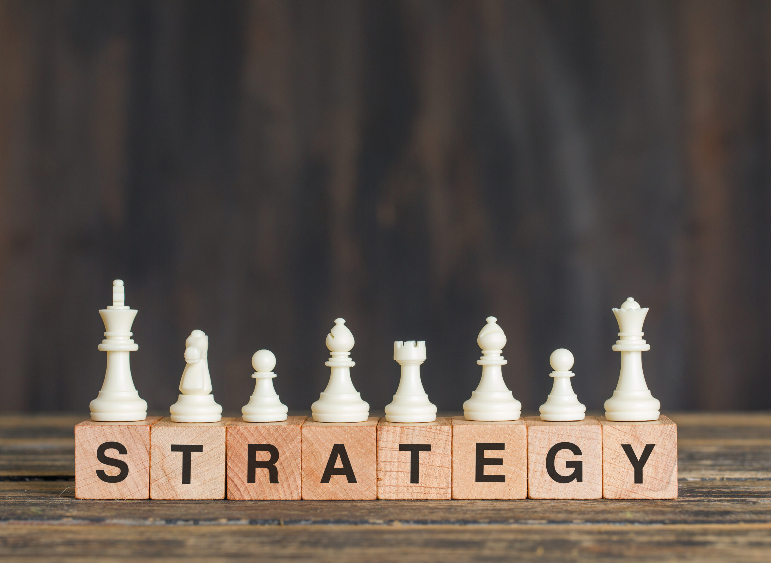 Business strategy concept with chess pieces on wooden cubes on wooden background side view.